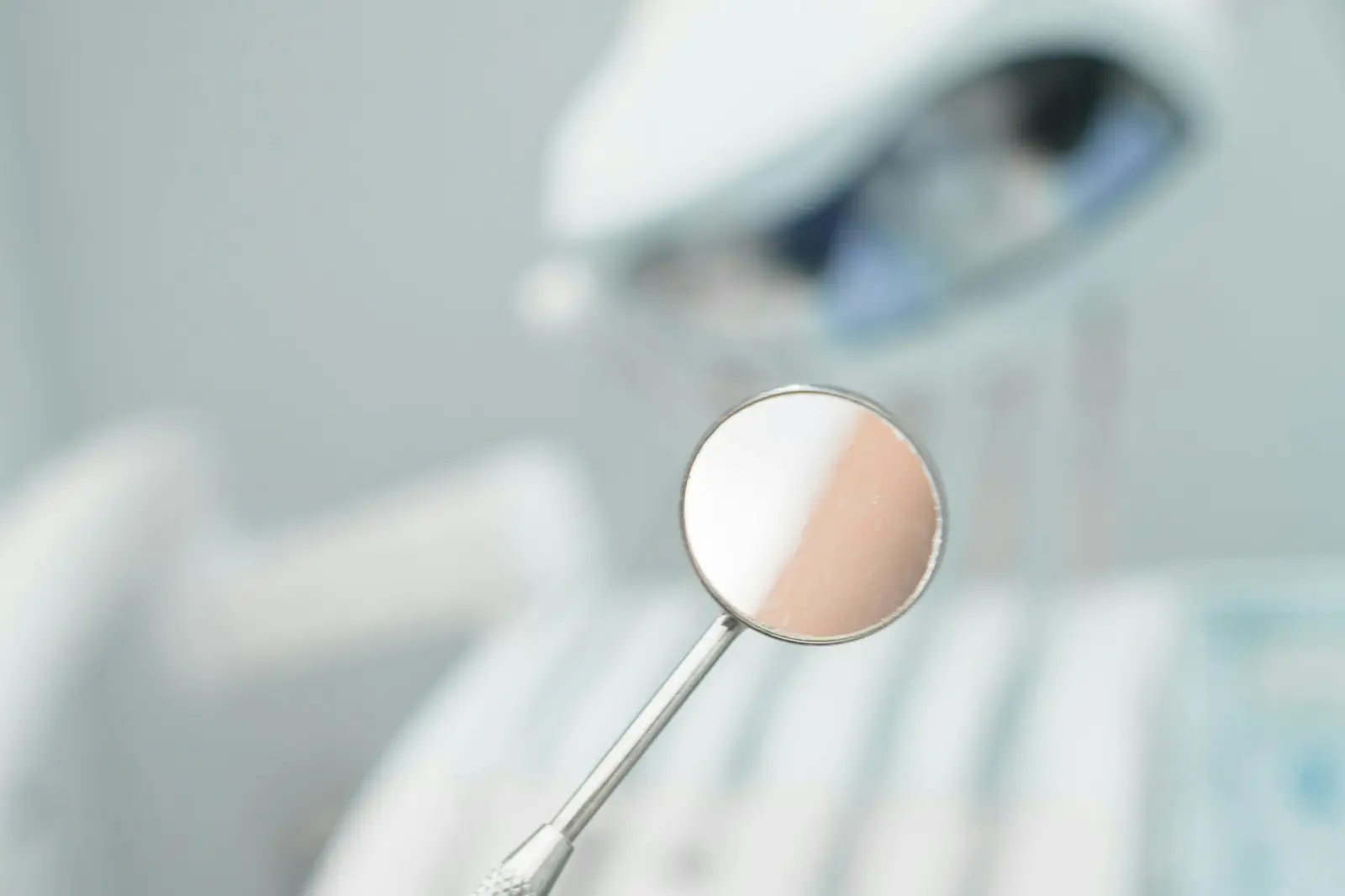A dental mirror held in the foreground of a treatment room